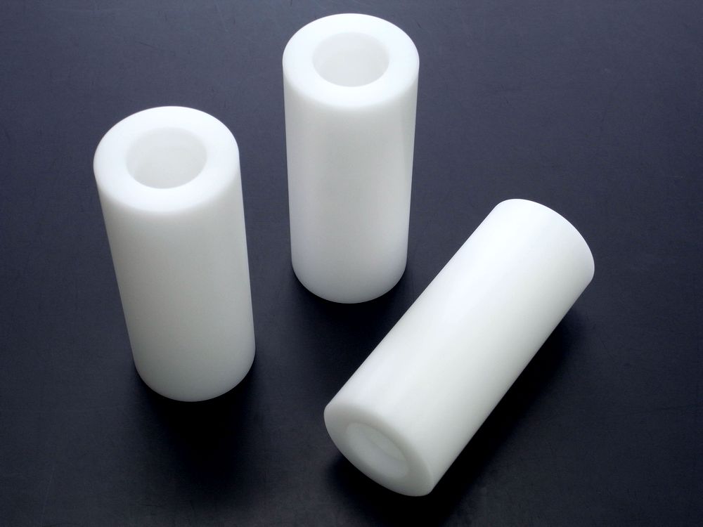 POM（ポリアセタール）白丸棒 φ50×120L の旋盤加工品。中央貫通穴と両端ザグリ、糸面取りC0.5、公差±0.05mmで精密切削。