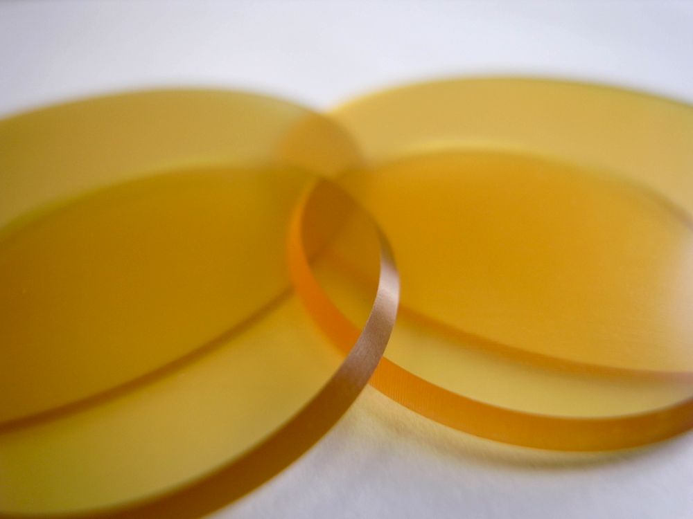 ウルテム1000（PEI）薄肉丸板φ32・φ55を重ね、琥珀色半透明の質感と切削面の仕上がりを強調したクローズアップ写真